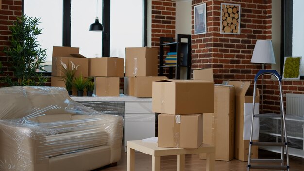 Nessuno nel soggiorno vuoto con imballaggi di cartone nella nuova casa, mobili in una pila di scatole di cartone. Nessuna persona in una proprietà domestica con un pacco da trasferire, immobili.