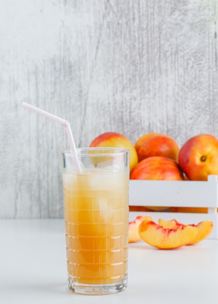 Nettarine con succo in una scatola di legno sulla parete bianca e grungy, vista laterale.