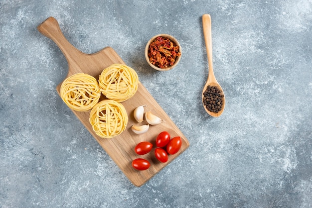 Nidi di pasta, aglio e pomodorini su tavola di legno.