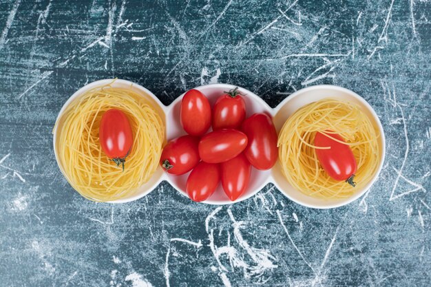 Nidi di spaghetti crudi con pomodori su sfondo blu. Foto di alta qualità