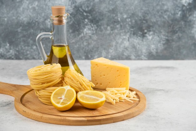 Nidi di spaghetti, olio, formaggio Lemonnd su tavola di legno.