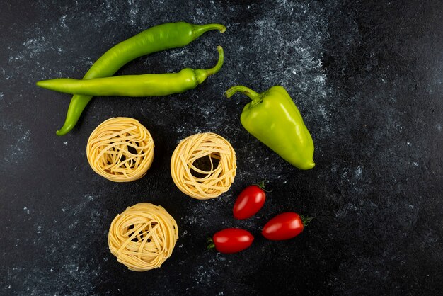 Nidi di tagliatelle crude e verdure su marmo.