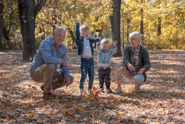 Nipoti e nonni che lanciano foglie nel parco e trascorrono del tempo insieme