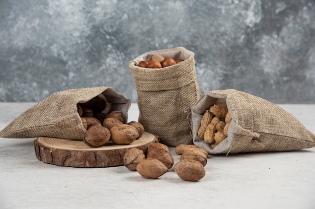 Nocciole sgusciate organiche, arachidi e noci in tela di sacco su tavola di marmo.