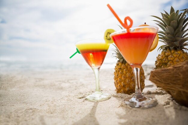 Noce di cocco, ananas e due bicchieri di cocktail tenuti sulla sabbia in spiaggia tropicale