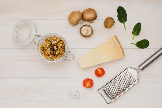 Noce; pomodori; formaggio; basilico e funghi con grattugia in metallo sulla scrivania in legno