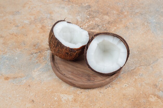 Noci di cocco mature tagliate a metà sul piatto di legno.