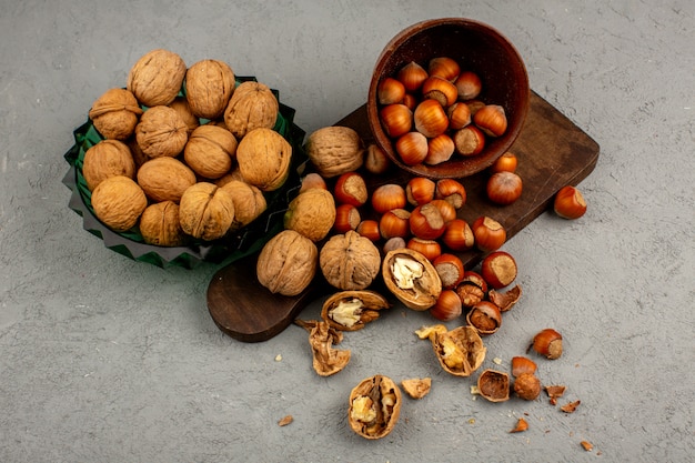 Noci e nocciole dentro il piatto verde e la pentola rotonda marrone intere e sbucciate su un gray