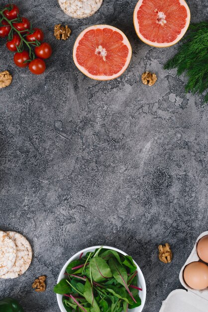 Noci; frutti d&#39;uva; torta di riso soffiato; spinaci; uova e pomodorini su sfondo grigio con texture