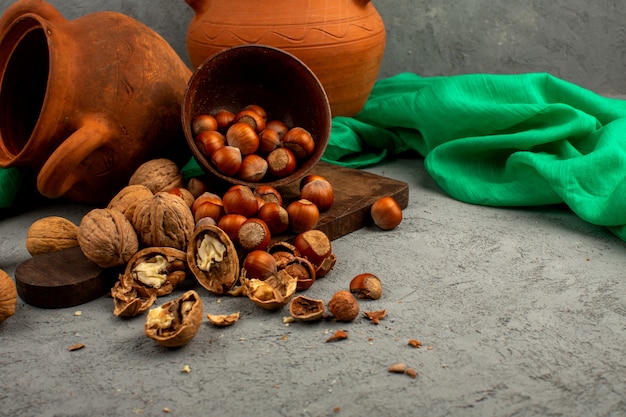 Noci marroni all'interno della pentola marrone intere e sbucciate insieme a tessuto verde e belle brocche su una scrivania grigia