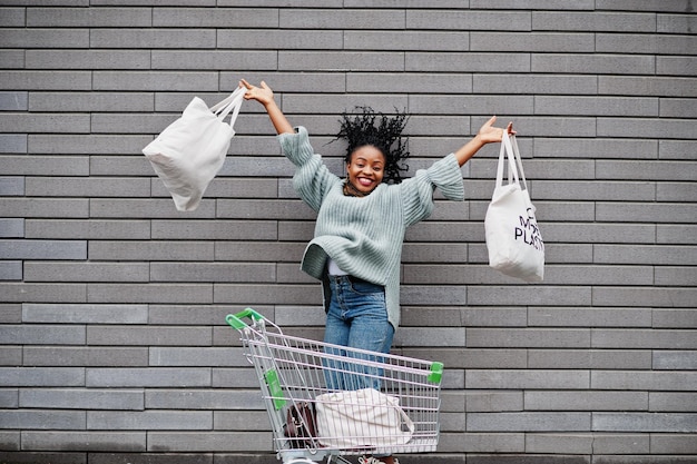 Non più donna africana di plastica con carrello del carrello e borse ecologiche salta il mercato all'aperto