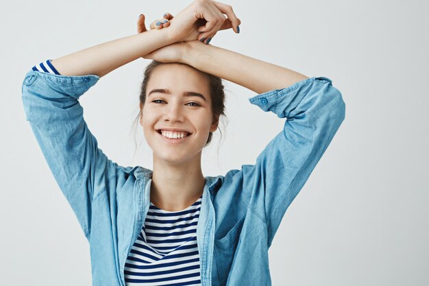 Non preoccuparti, sii felice. Ritratto della bellissima fidanzata innamorata, tenendo le braccia incrociate sulla fronte, in piedi in una posa sensuale, sorridendo ampiamente ed esprimendo emozioni positive e tenere.