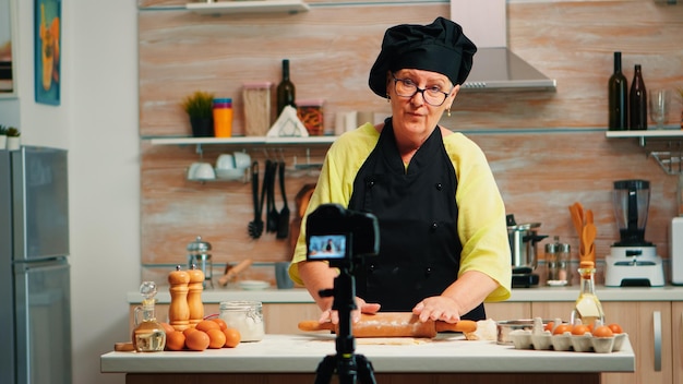 Nonna che fa vlog di cucina, registrandosi sulla macchina fotografica. Influencer chef blogger in pensione che utilizza la tecnologia Internet per comunicare, fotografare blog sui social media con apparecchiature digitali