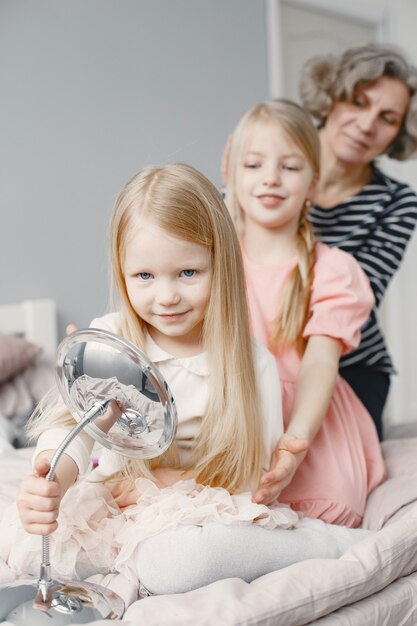 Nonna che intreccia i capelli della nipote. Seconda sorella che intreccia la nipote. Casa accogliente, relazioni familiari.