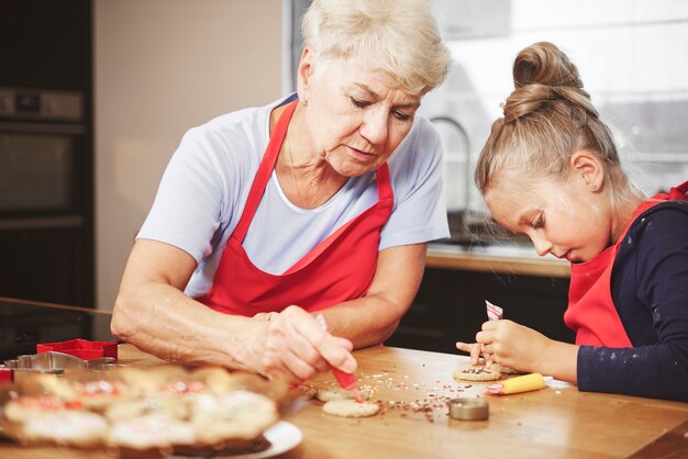 Nonna con ragazza cuocere e decorare i biscotti insieme