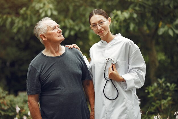 Nonno con sedia a rotelle assistito da infermiera all'aperto. Uomo anziano e giovane badante nel parco.