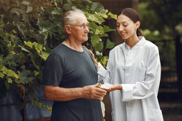 Nonno con sedia a rotelle assistito da infermiera all'aperto. Uomo anziano e giovane badante nel parco.