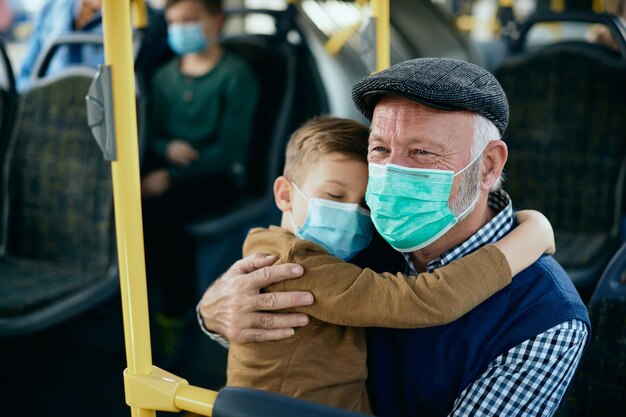 Nonno premuroso con nipote che indossa maschere per il viso mentre si sposta in autobus