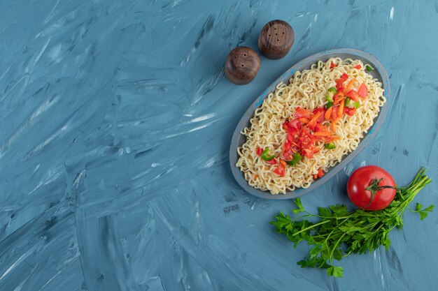 Noodle e insalata su un piatto di legno accanto a prezzemolo e pomodori, sullo sfondo di marmo.