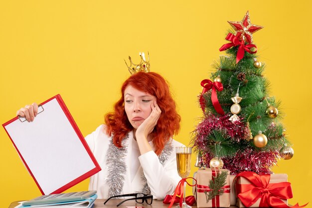 Nota di archivio femminile della tenuta del medico di vista frontale intorno all'albero di natale ed ai regali