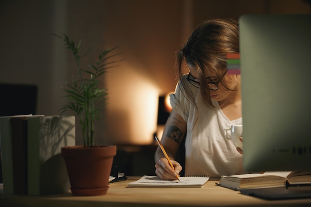 Note concentrate di scrittura del progettista della giovane donna facendo uso del computer