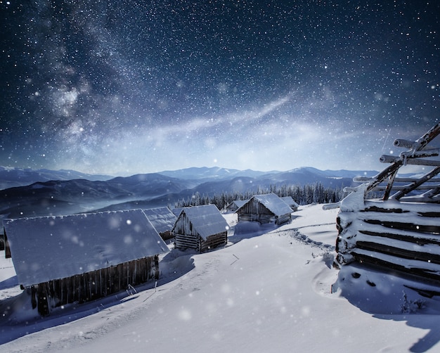 Notte con le stelle. Paesaggio natalizio. Casa in legno nel villaggio di montagna. Paesaggio notturno in inverno