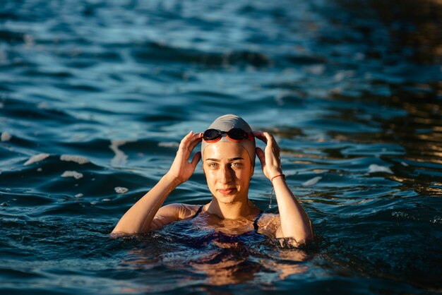 Nuotatore femminile con cappuccio e occhiali in posa mentre nuota in acqua