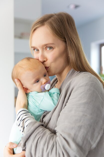 Nuova madre positiva che bacia e che stringe a sé bambino