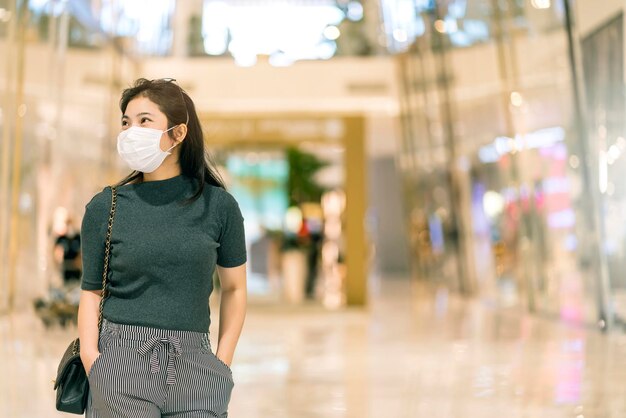 Nuova normalità dopo l'epidemia di covid giovane donna asiatica d'affari che indossa una maschera di protezione facciale che cammina nel centro commerciale del centro commerciale della piazza del grande magazzino nuovo stile di vita dopo la diffusione del virus corona covid19