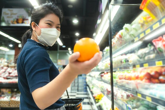 Nuova normalità dopo l'epidemia di covid giovane donna asiatica intelligente shopping nuovo stile di vita nel supermercato con protezione facciale o maschera mano scegli prodotti di consumo nuovo stile di vita normale