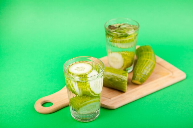 Nutriente acqua disintossicante fatta in casa dai cetrioli organici in due bicchieri su uno sfondo verde