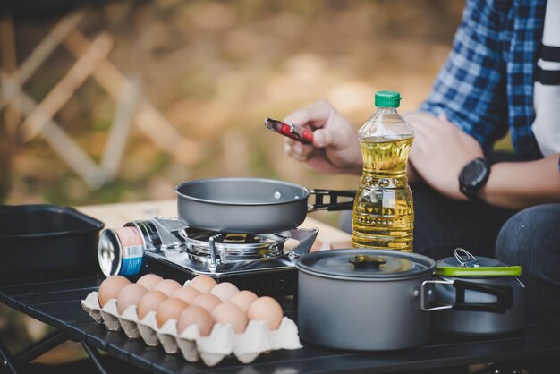 Occhiali da uomo viaggiatore asiatico che friggono un gustoso uovo fritto in una padella calda al campeggio Cucina all'aperto concetto di stile di vita in campeggio in viaggio