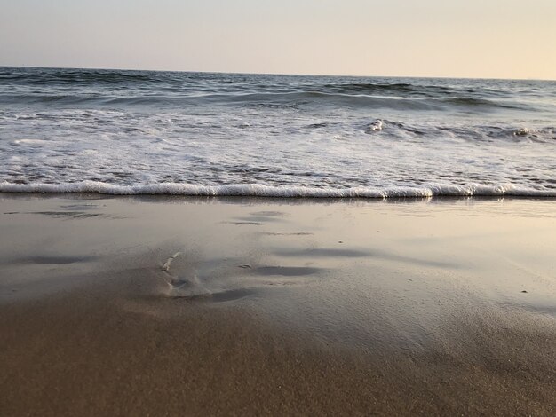 Oceano ondulato che colpisce la spiaggia sabbiosa e luccica sotto il cielo colorato