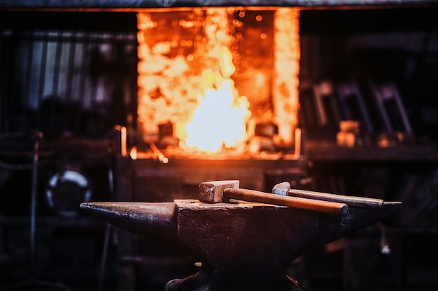 Officina stithy scura con martello sull'incudine al piano degli abeti e fuoco nella stufa sullo sfondo.