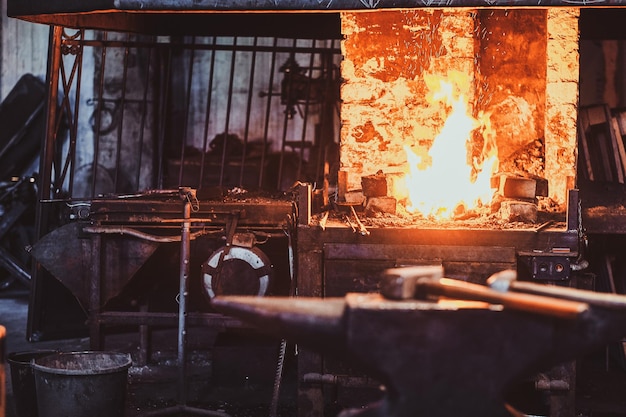 Officina stithy scura con martello sull'incudine al piano degli abeti e fuoco nella stufa sullo sfondo.