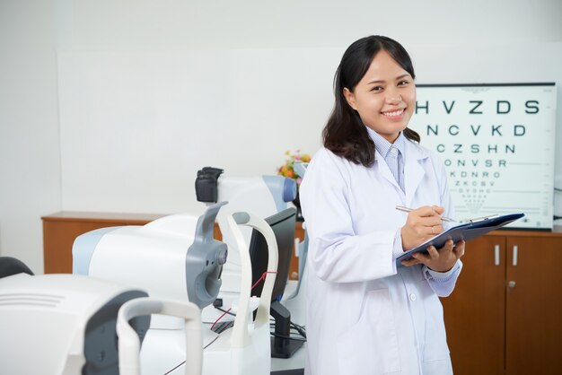 Oftalmologo asiatico che sta nella stanza dell'esame vicino alle macchine di prova di vista