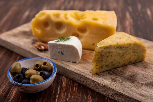 Olive di vista laterale con varietà di formaggio su un supporto su un fondo di legno