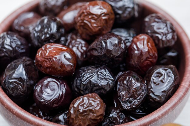 Olive nere e kalamata in una ciotola dell'argilla su bianco. avvicinamento.