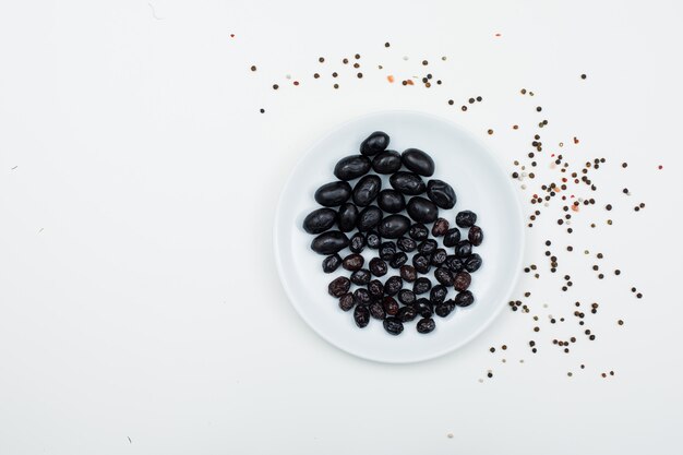 Olive nere in un piatto bianco con la vista superiore delle spezie su bianco