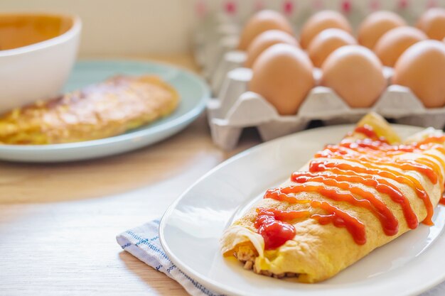 Omelette con ketchup in cima a un piatto bianco con un vassoio di uova sfocatura come sfondo
