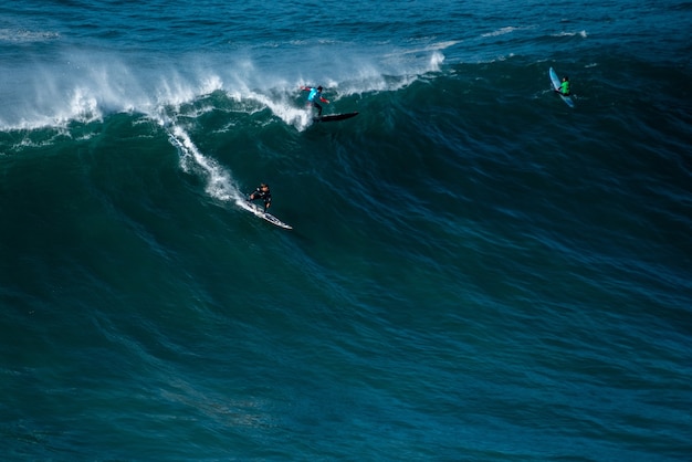 Onda alta dell'Oceano Atlantico che trasporta i surfisti verso la riva di Nazare, Portogallo