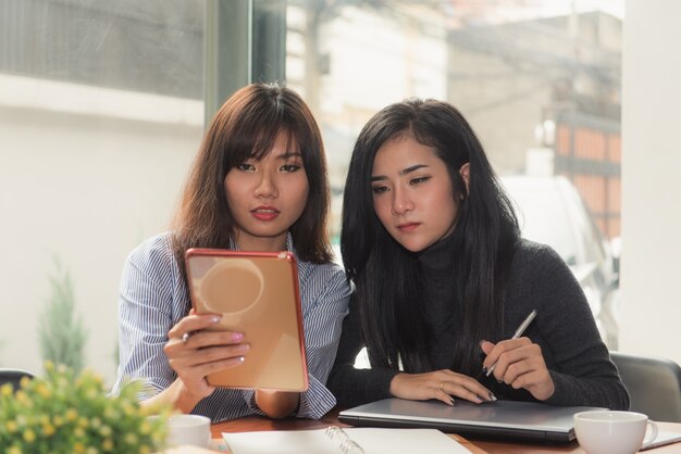 One-on-one meeting.Two giovani donne d&#39;affari seduti a tavola in caffè. La ragazza mostra informazioni sul collega sullo schermo del computer portatile. Ragazza utilizzando smartphone blogging. Riunione di lavoro di squadra. Liberi professionisti che lavorano.