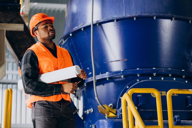 Operaio afroamericano in piedi in uniforme che indossa un cappello di sicurezza in una fabbrica