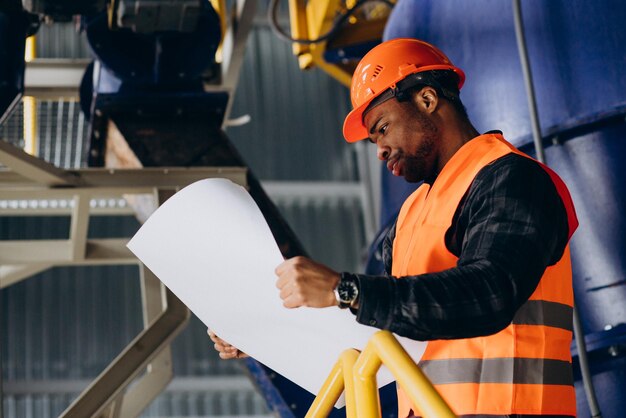 Operaio afroamericano in piedi in uniforme che indossa un cappello di sicurezza in una fabbrica