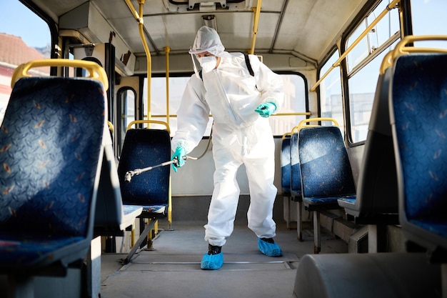 Operaio disinfettante che spruzza all'interno di un autobus pubblico a causa della pandemia di coronavirus