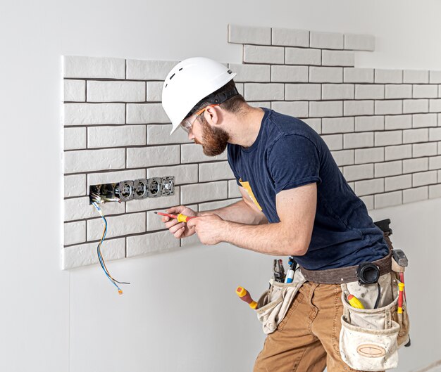 Operaio edile elettricista con la barba in tuta durante l'installazione delle prese. Concetto di ristrutturazione della casa.