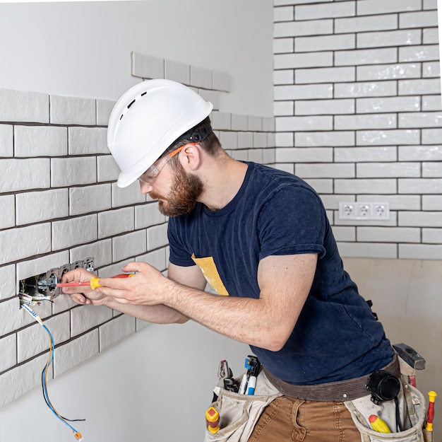 Operaio edile elettricista con la barba in tuta durante l'installazione delle prese. Concetto di ristrutturazione della casa.