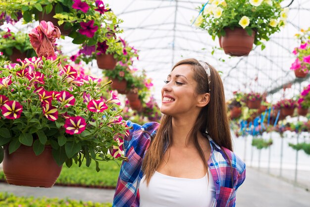 Operaio femminile della scuola materna del fiorista che tiene i fiori in vaso e che sorride nel centro del giardino