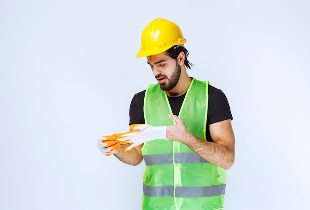 Operaio in casco giallo che tira fuori e dimostra i suoi guanti da officina.