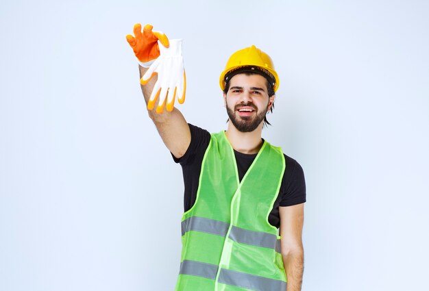 Operaio in casco giallo che tira fuori e dimostra i suoi guanti da officina.